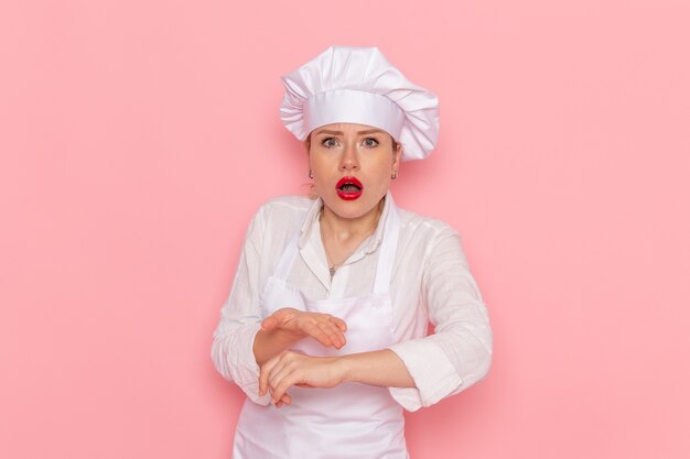 Vue de face de la pâtissière en vêtements blancs vérifiant son poignet sur le travail de travail de pâtisserie sucrée confiserie bureau rose clair