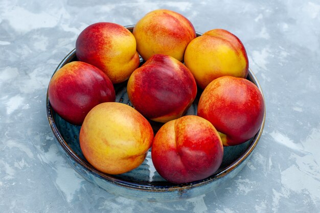 Vue de face pêches fraîches délicieux fruits d'été sur un bureau blanc clair