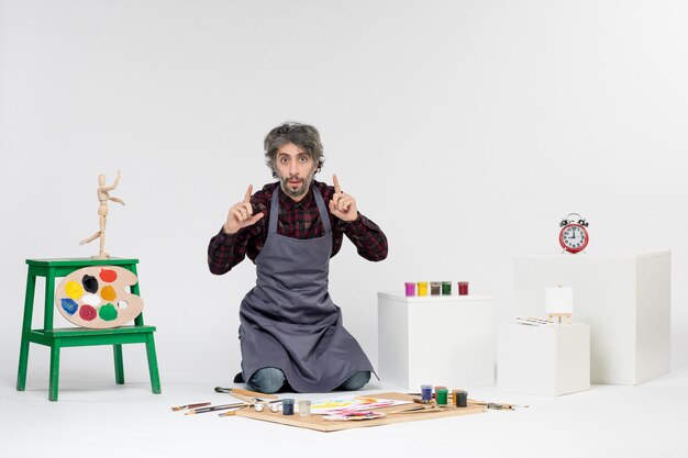Photo gratuite vue de face peintre masculin assis avec des peintures et des glands sur fond blanc art couleur travail temps photo artiste dessiner peinture