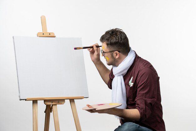 Vue de face peintre masculin dessin sur chevalet avec pinceau et peintures sur mur blanc