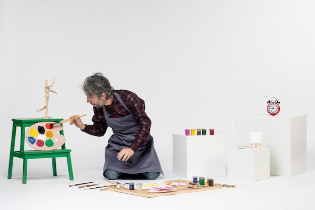 Vue de face peintre masculin à l'intérieur de la chambre avec des peintures et des pinceaux sur fond blanc couleurs peinture photo dessiner artiste travail d'art