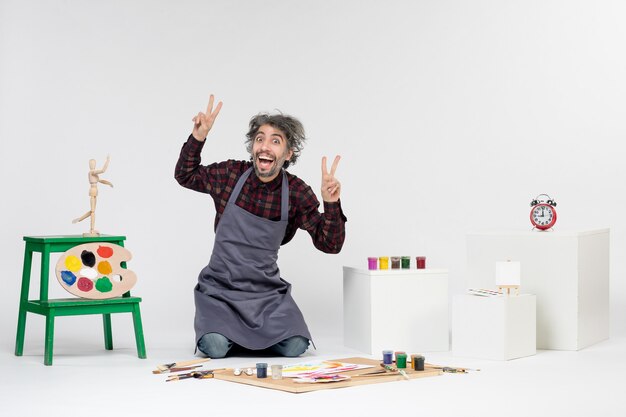 Vue de face peintre masculin à l'intérieur de la pièce pleine de peintures et de glands pour dessiner sur fond blanc dessin couleur peinture photo d'art