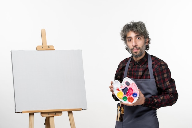 Vue de face peintre masculin tenant des peintures et se préparant à dessiner sur un mur blanc