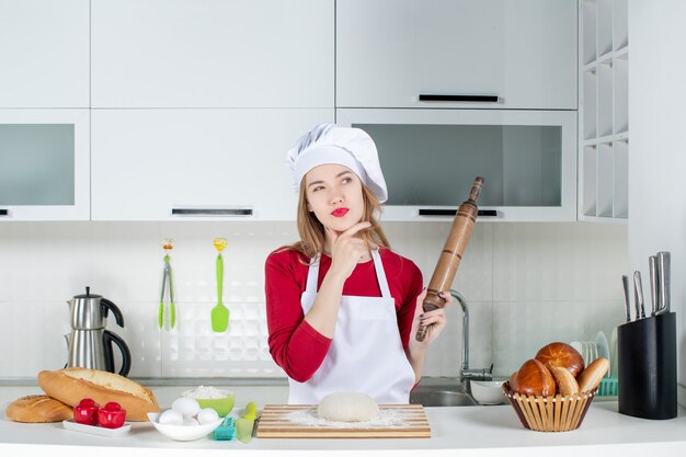 Vue de face pensant chef féminin tenant un rouleau à pâtisserie dans la cuisine