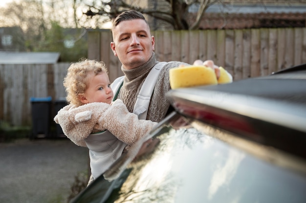 Photo gratuite vue de face père avec bébé laver la voiture