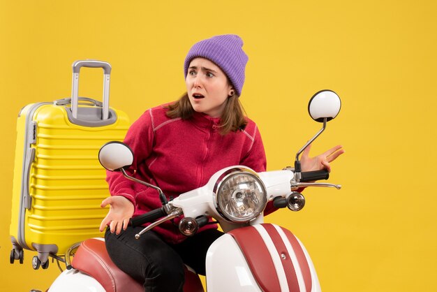 Vue de face perplexe jeune fille en pull rouge sur cyclomoteur