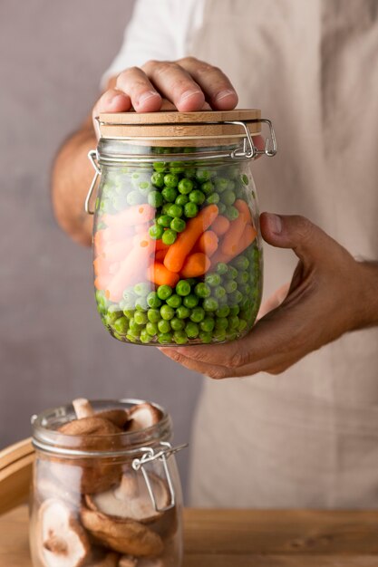 Vue de face de la personne tenant des pois et des carottes dans un bocal en verre