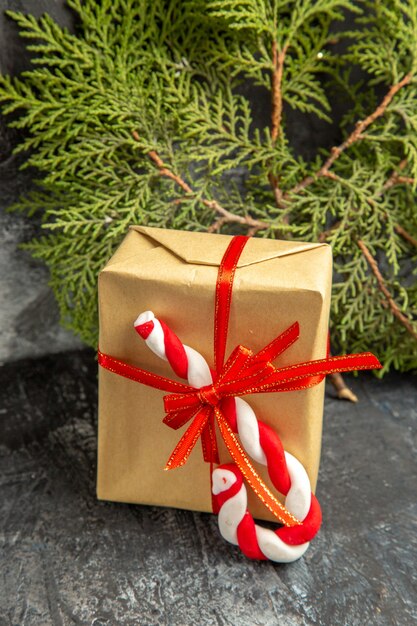 Vue de face petit cadeau attaché avec des branches de pin bonbon de Noël ruban rouge sur fond gris