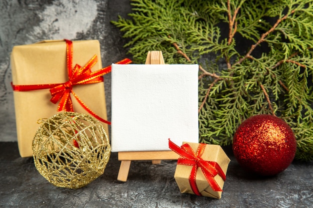 Vue de face petit cadeau noué avec une mini toile de ruban rouge sur des boules de Noël de branche de pin de chevalet sur fond gris