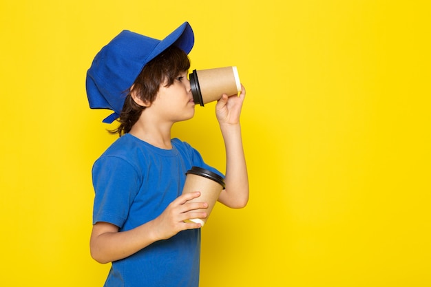 Une vue de face petit coursier mignon en t-shirt bleu casquette bleue tenant des tasses à café