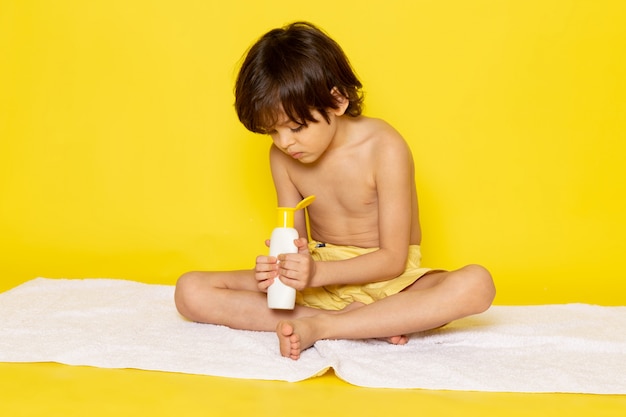 vue de face petit enfant à l'aide de crème sur sol jaune