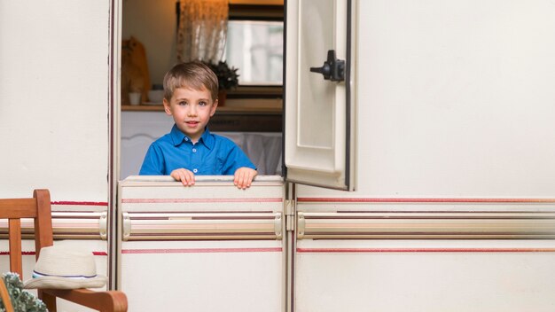 Vue de face petit garçon debout devant la porte d'une caravane