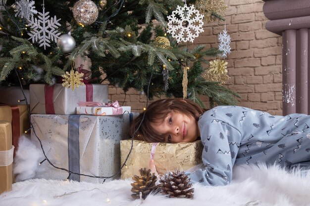Vue de face petit garçon mignon en pyjama allongé autour de l'arbre de Noël et présente
