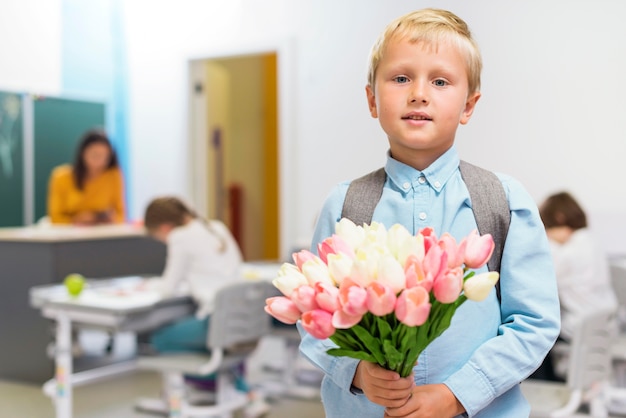 Photo gratuite vue de face petit garçon tenant un bouquet de fleurs pour son professeur