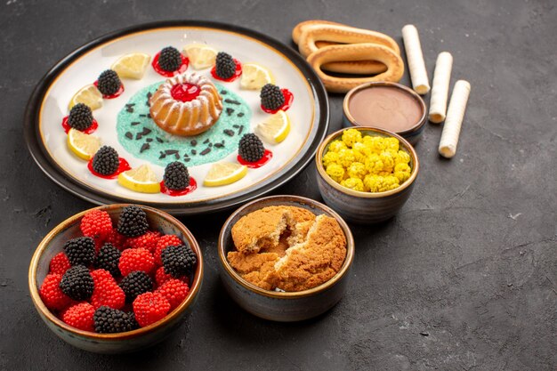 Vue de face petit gâteau aux biscuits avec des tranches de citron et des bonbons sur fond sombre gâteau biscuit aux agrumes biscuit sucré