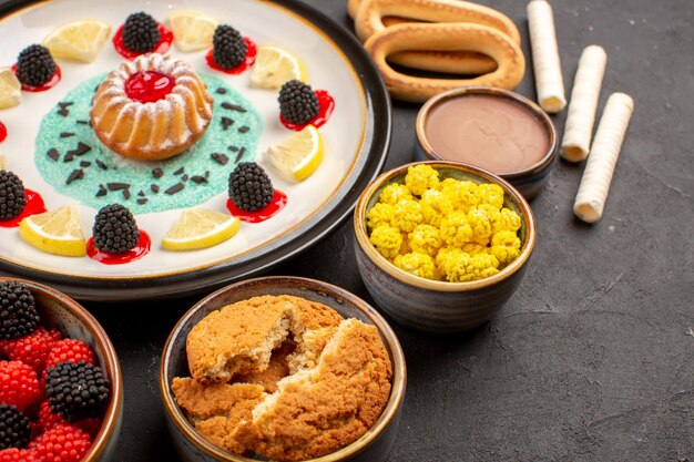 Vue de face petit gâteau aux biscuits avec des tranches de citron et des bonbons sur fond sombre gâteau biscuit aux agrumes biscuits sucrés