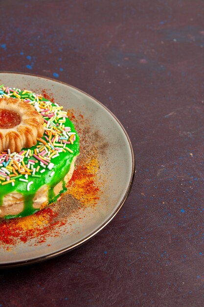 Vue de face petit gâteau délicieux avec de la crème verte sur le mur sombre biscuit biscuit gâteau au sucre sucré tarte