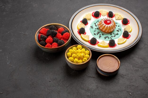 Photo gratuite vue de face petit gâteau délicieux avec des tranches de citron et des bonbons sur fond sombre biscuit aux agrumes aux fruits sucré