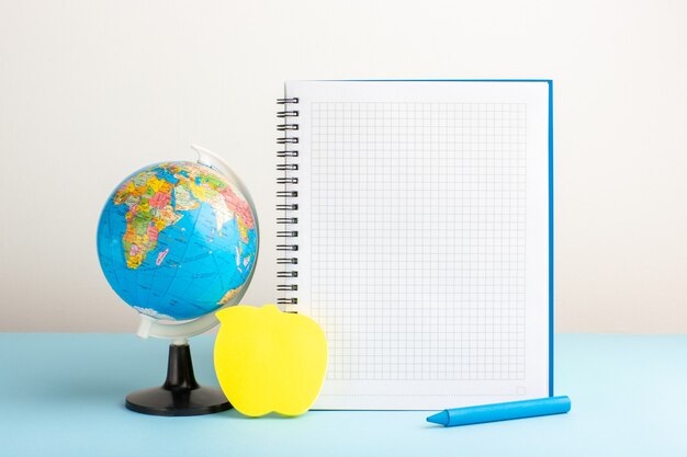 Vue de face petit globe terrestre avec cahier sur bureau bleu