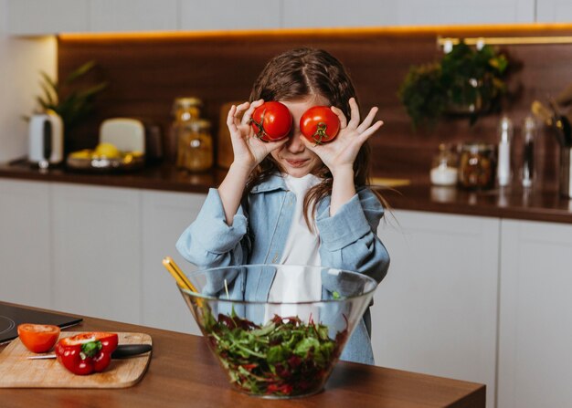Vue de face de la petite fille dans la cuisine avec des tomates
