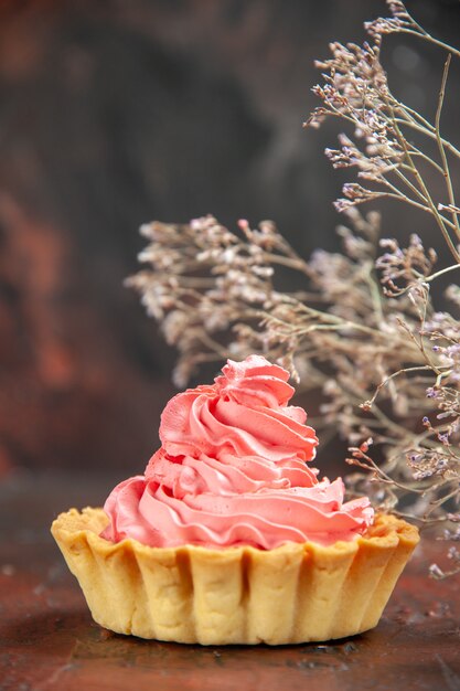 Vue de face petite tarte à la crème pâtissière rose branche de fleurs séchées sur table rouge foncé