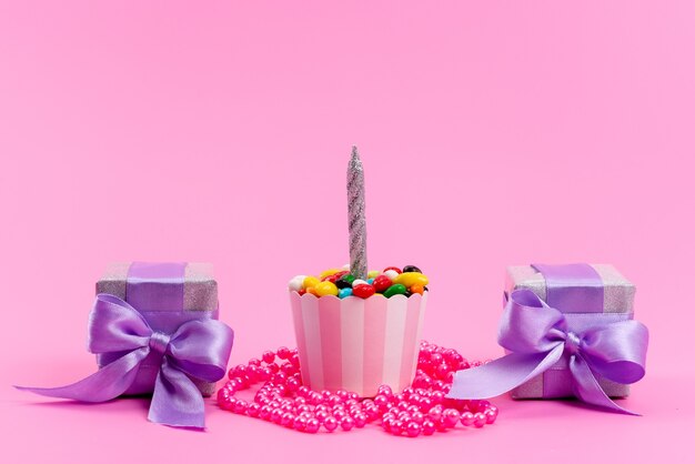 Une vue de face de petites boîtes violettes avec des bonbons colorés et des bougies sur rose, sucre biscuit sucré anniversaire