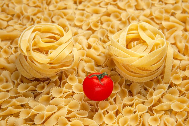 Vue de face de petites pâtes crues sur de la lumière beaucoup de pâte photo couleur de repas de nourriture