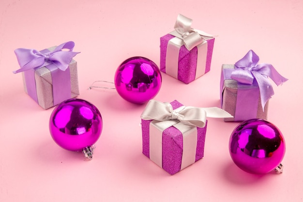 Vue de face de petits cadeaux avec des jouets d'arbre de noël sur la table rose