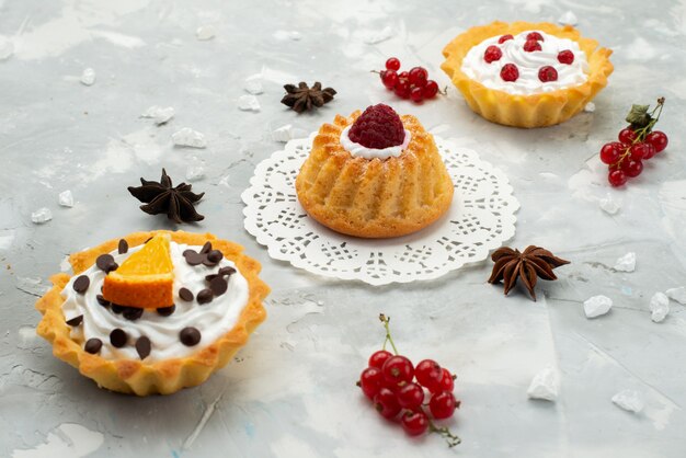 Vue de face de petits gâteaux à la crème et différents fruits isolés sur la surface légère du sucre sucré thé