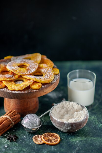 Vue de face de petits gâteaux délicieux en forme d'anneau d'ananas avec du lait sur la surface sombre