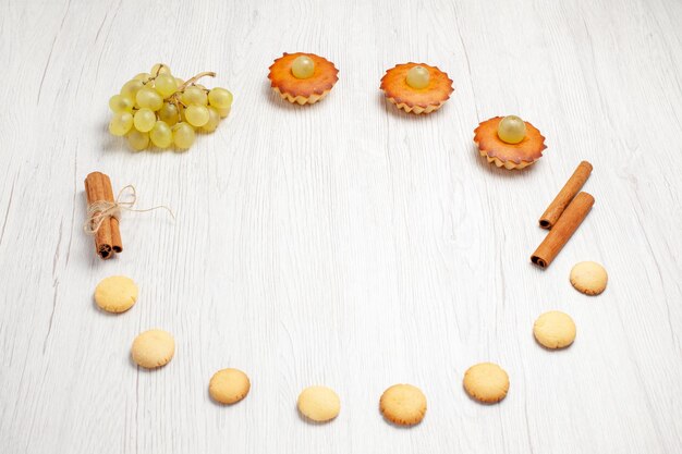 Vue de face de petits gâteaux délicieux avec des raisins et des biscuits sur un bureau blanc gâteau aux fruits biscuit dessert sucré thé