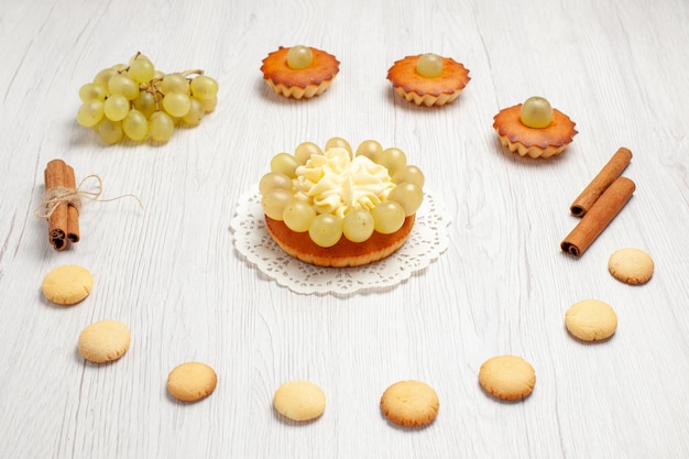 Vue de face de petits gâteaux délicieux avec des raisins et des biscuits sur un gâteau de bureau blanc biscuit dessert sucré