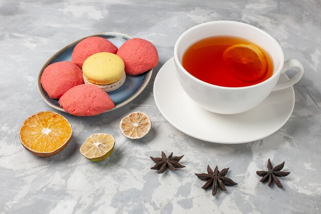 Vue de face petits gâteaux délicieux avec tasse de thé sur une surface blanche