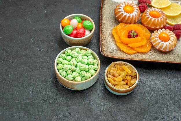 Vue de face de petits gâteaux délicieux avec des tranches de citron mandarines et des bonbons sur un espace sombre