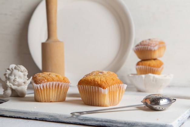 Vue de face de petits gâteaux à l'intérieur de formulaires papier avec du sucre en poudre sur le bureau blanc