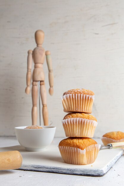 Vue de face de petits gâteaux à l'intérieur de formulaires papier avec du sucre en poudre sur la surface blanche