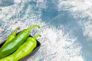 Photo gratuite vue de face des piments verts sur une plaque noire sur un espace libre bleu-blanc