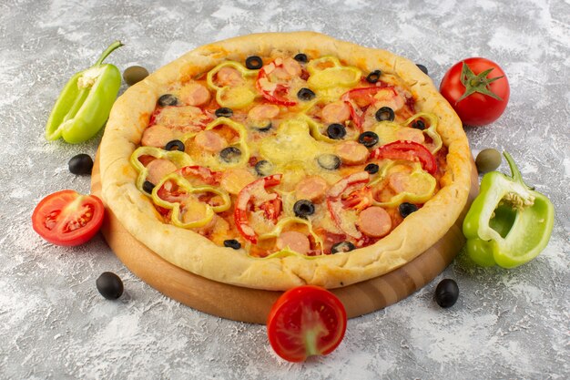 Vue de face de la pizza au fromage avec olives, saucisses et tomates rouges sur le bureau gris