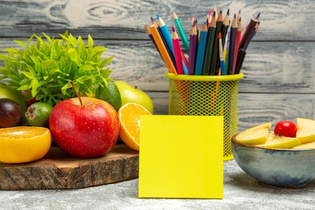 Vue de face des pommes fraîches avec des tranches d'oranges et des crayons sur fond gris fruits mûrs mûrs pomme fraîche