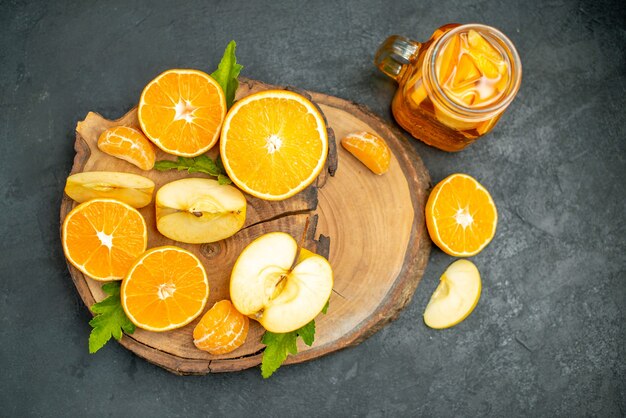 Vue de face des pommes et des oranges coupées sur un cocktail de planche de bois dans l'obscurité