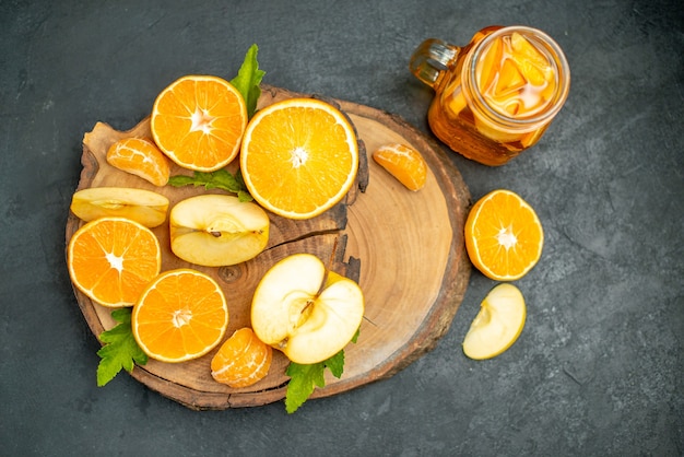 Vue de face des pommes et des oranges coupées sur un cocktail de planche de bois sur fond sombre