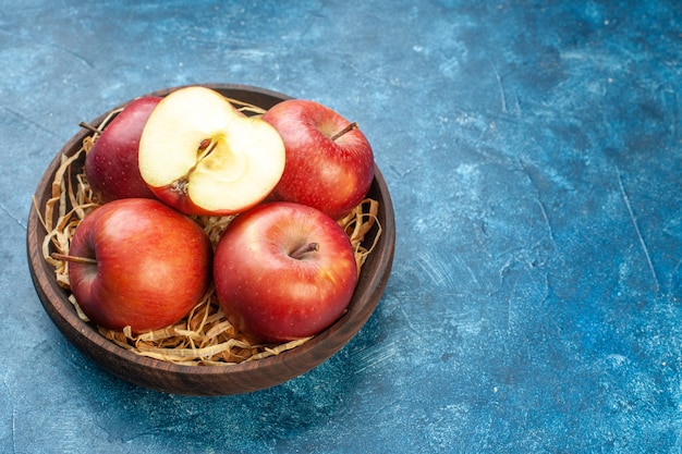 Photo gratuite vue de face des pommes rouges fraîches à l'intérieur de la plaque sur la surface bleue