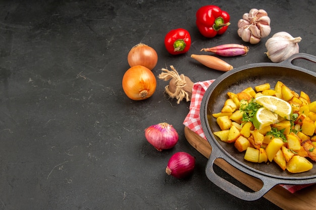 Vue de face des pommes de terre frites à l'intérieur de la poêle avec des légumes frais sur une table sombre