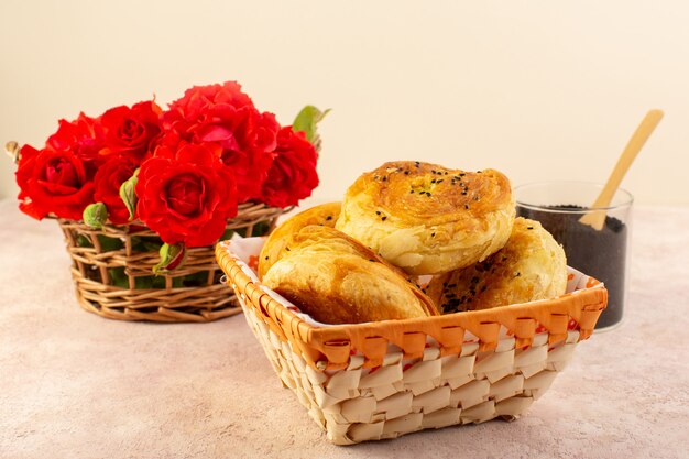 Une vue de face qogals cuits au four petits pains cuits au four frais chaud à l'intérieur du bac à pain avec fleurs rouges et poivre sur table et rose