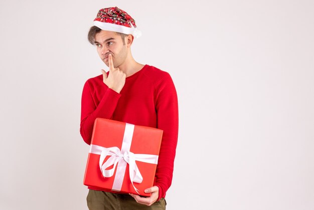 Vue de face réfléchie jeune homme avec bonnet de Noel debout sur blanc