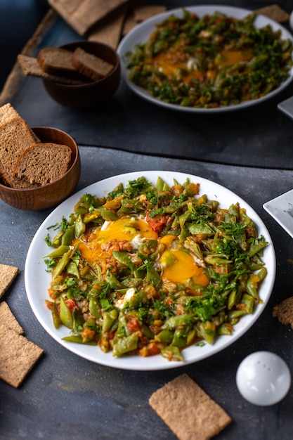 Une vue de face repas de légumes en tranches savoureux coloré à l'intérieur de la plaque blanche avec des œufs chips sur la table grise plat légumes