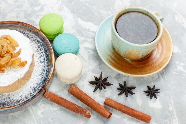 Vue de face ronde petit gâteau de sucre en poudre avec du thé aux raisins secs et macarons français sur bureau blanc sucre gâteau biscuit sucré tarte à la crème