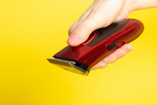 Une vue de face rouge foncé machine machine à cheveux mécanique dans la main de la jeune femme sur le fond jaune équipement de coiffeur