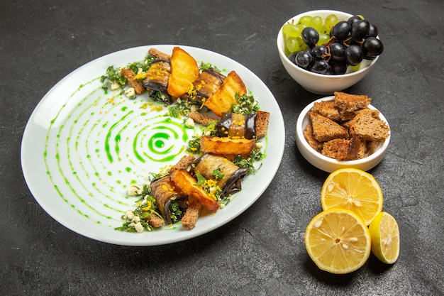 Vue de face des rouleaux d'aubergines cuites avec des raisins et des tranches de citron sur fond sombre plat dîner repas cuisson des fruits