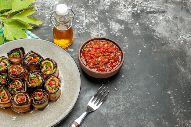 Vue de face des rouleaux d'aubergines farcies dans une assiette ovale blanche à l'huile de fourchette adjika dans un petit bol sur fond gris place libre